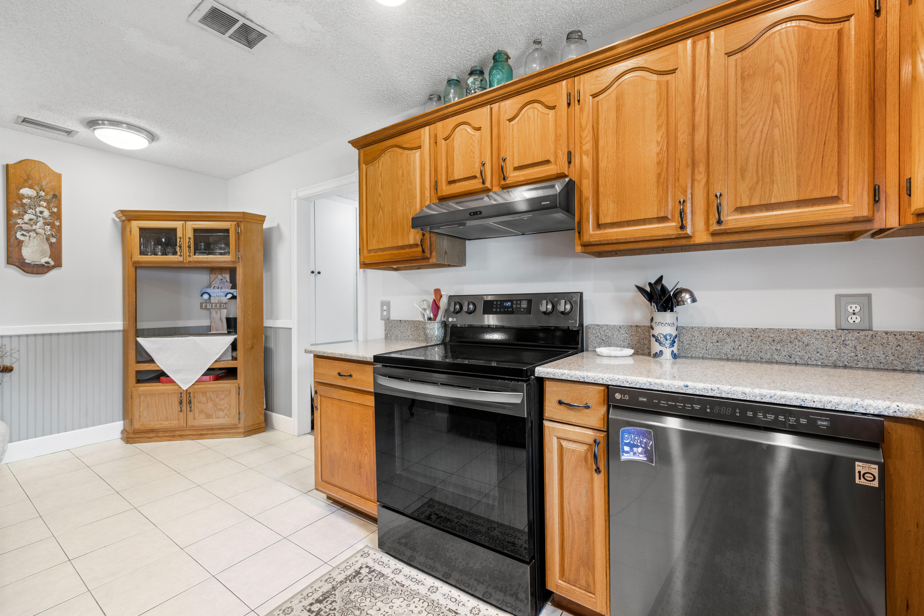 Kitchen with honey-colored wood cabinets, black range, speckled counters, and stainless dishwasher.