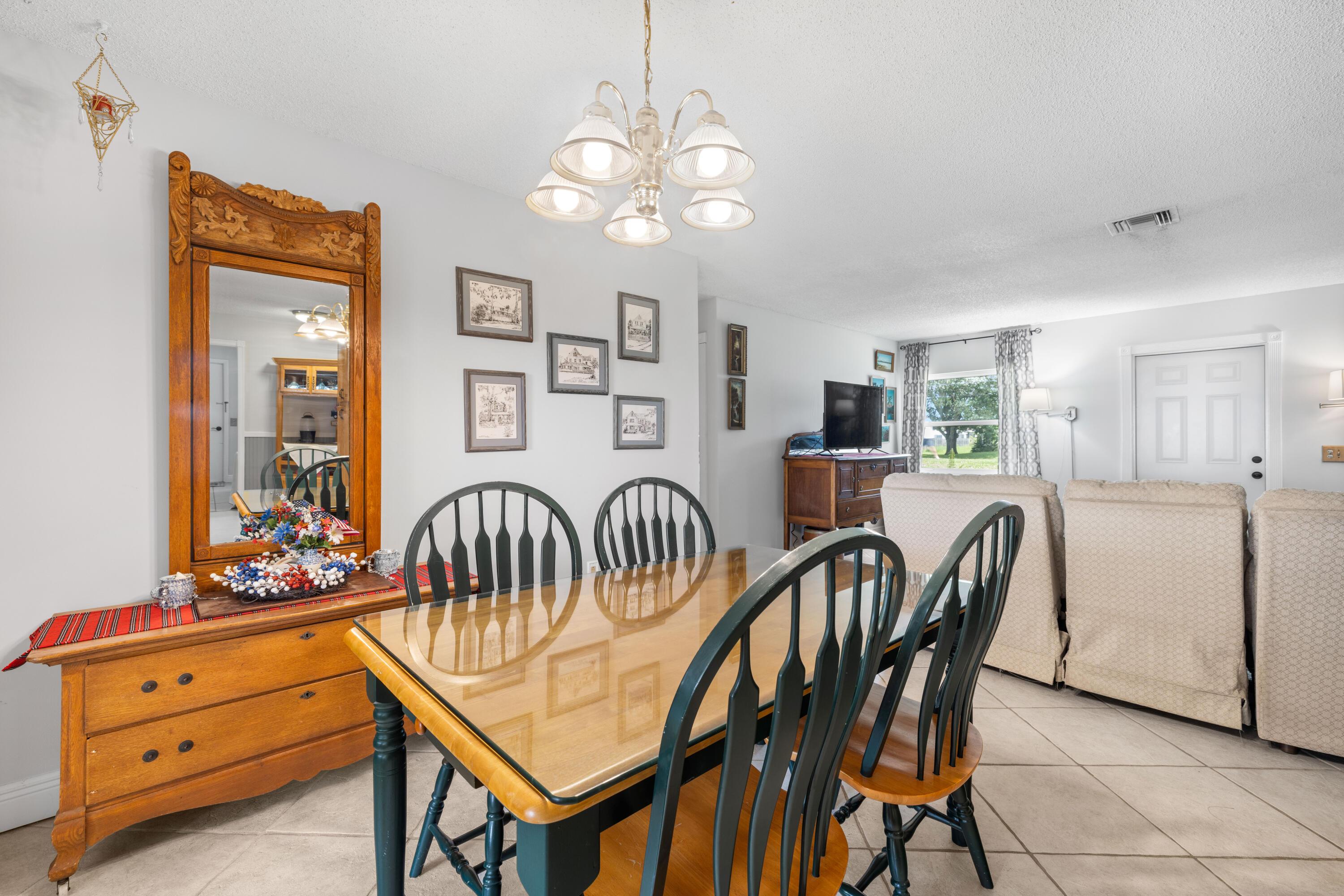 Dining area with a glass-top table and dark chairs beside a carved wooden sideboard and mirror.