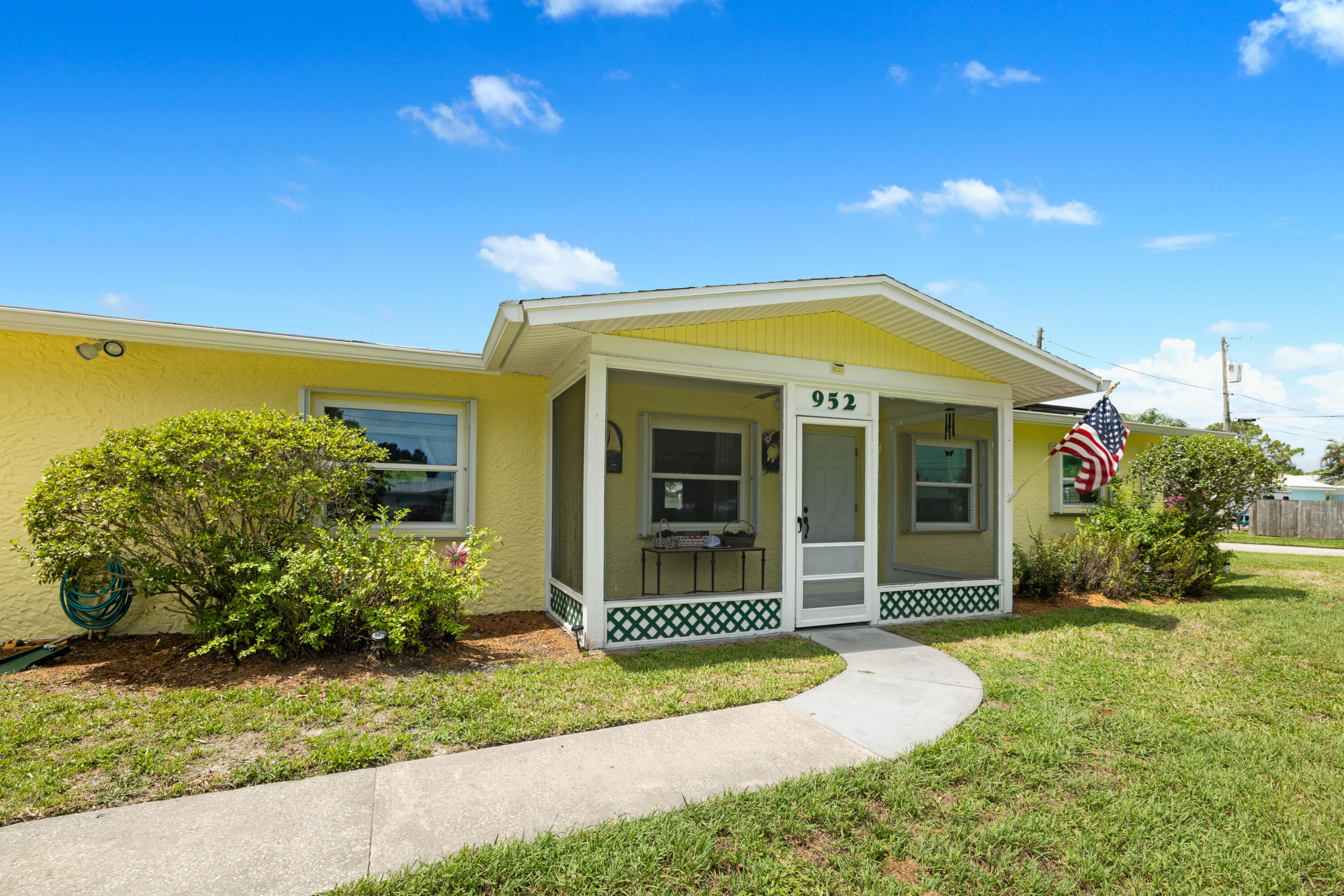 Yellow single-story home with a screened porch, curved walkway, and American flag.