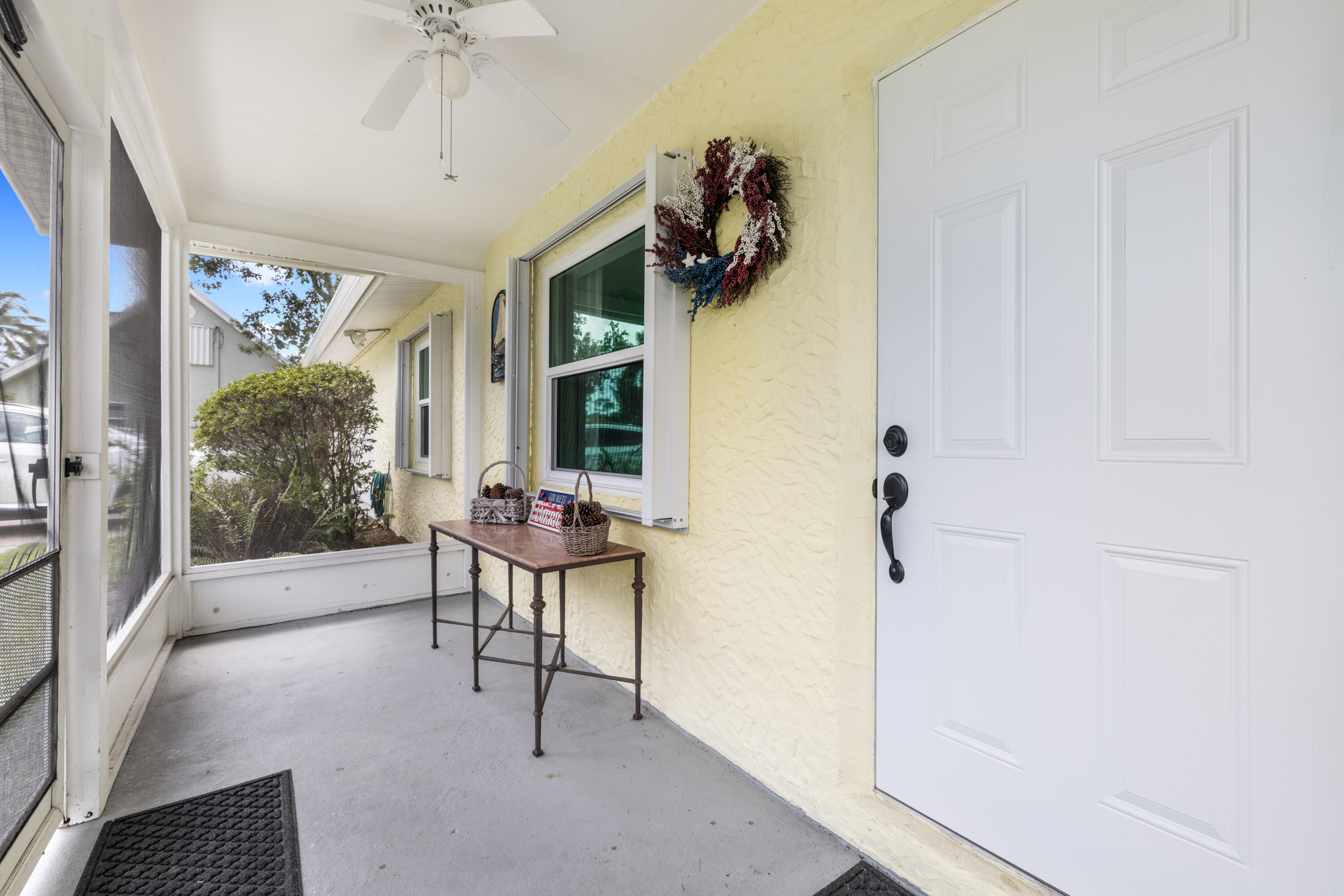 Screened front porch with a white entry door, yellow stucco walls, and a small console table.