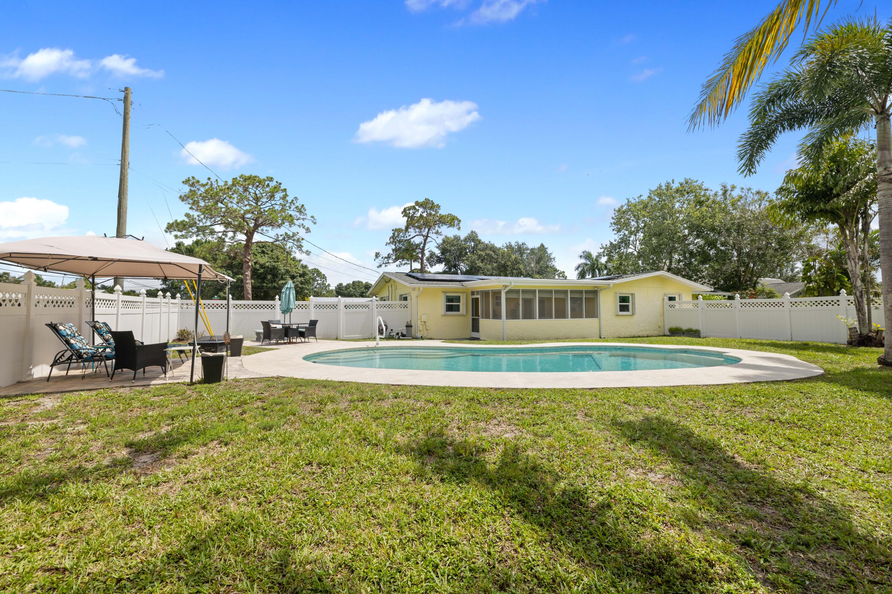 Yellow home with a curved backyard pool, white fencing, and shaded patio seating.