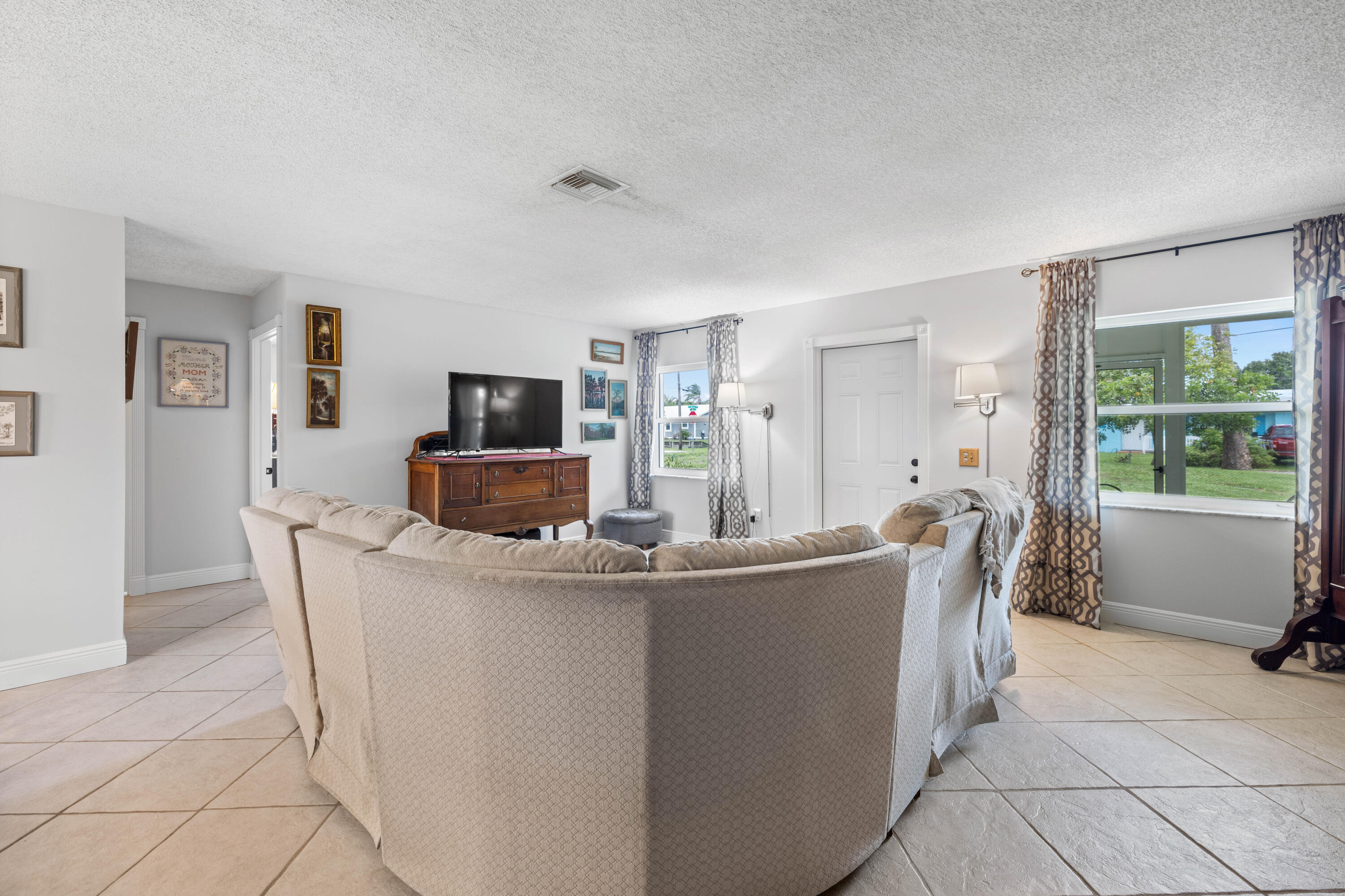 Living room with a curved beige sectional, tiled floors, and a television on a wooden console.
