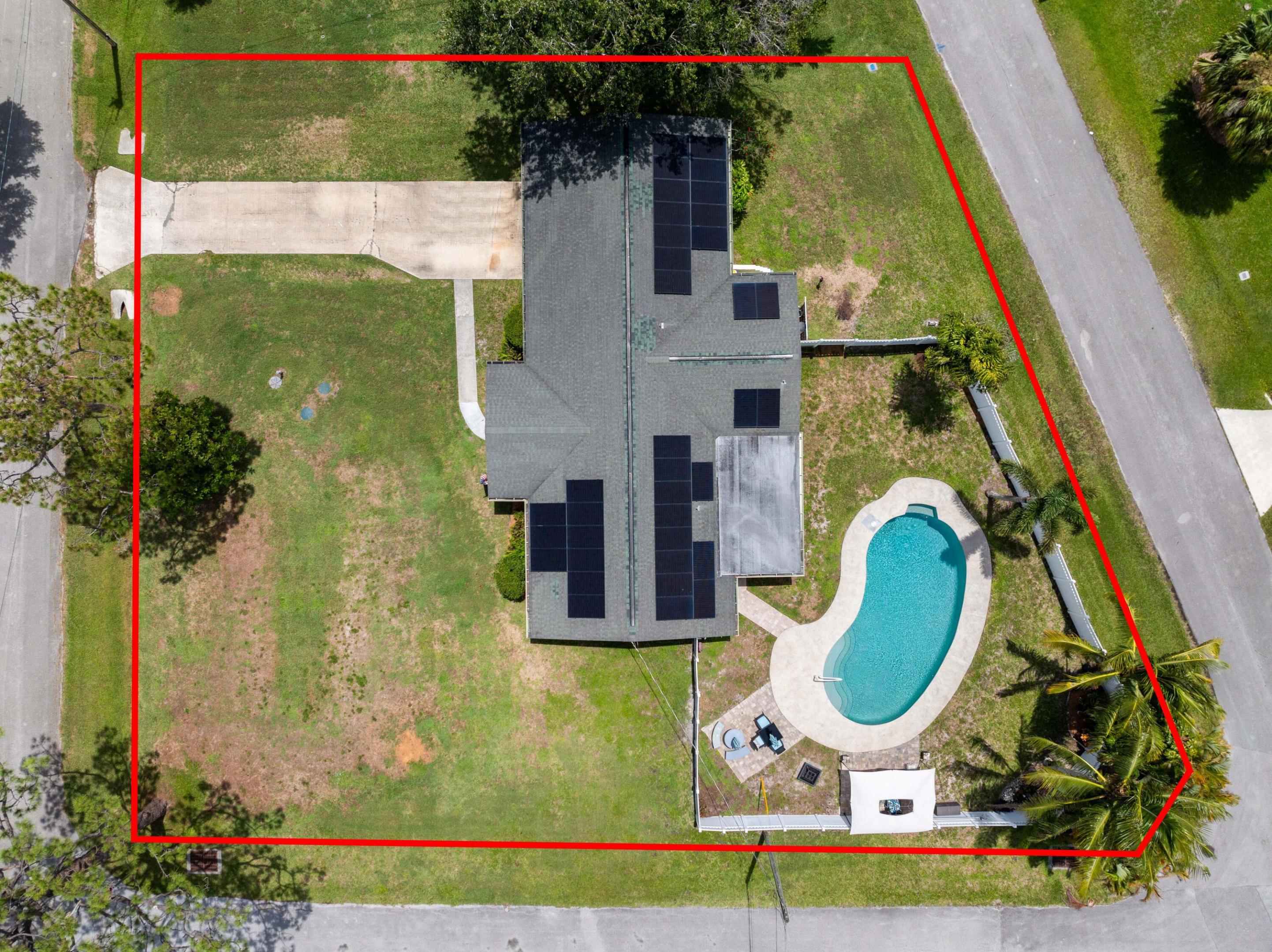 Aerial view of a home with rooftop solar panels and a curved pool, outlined in red.