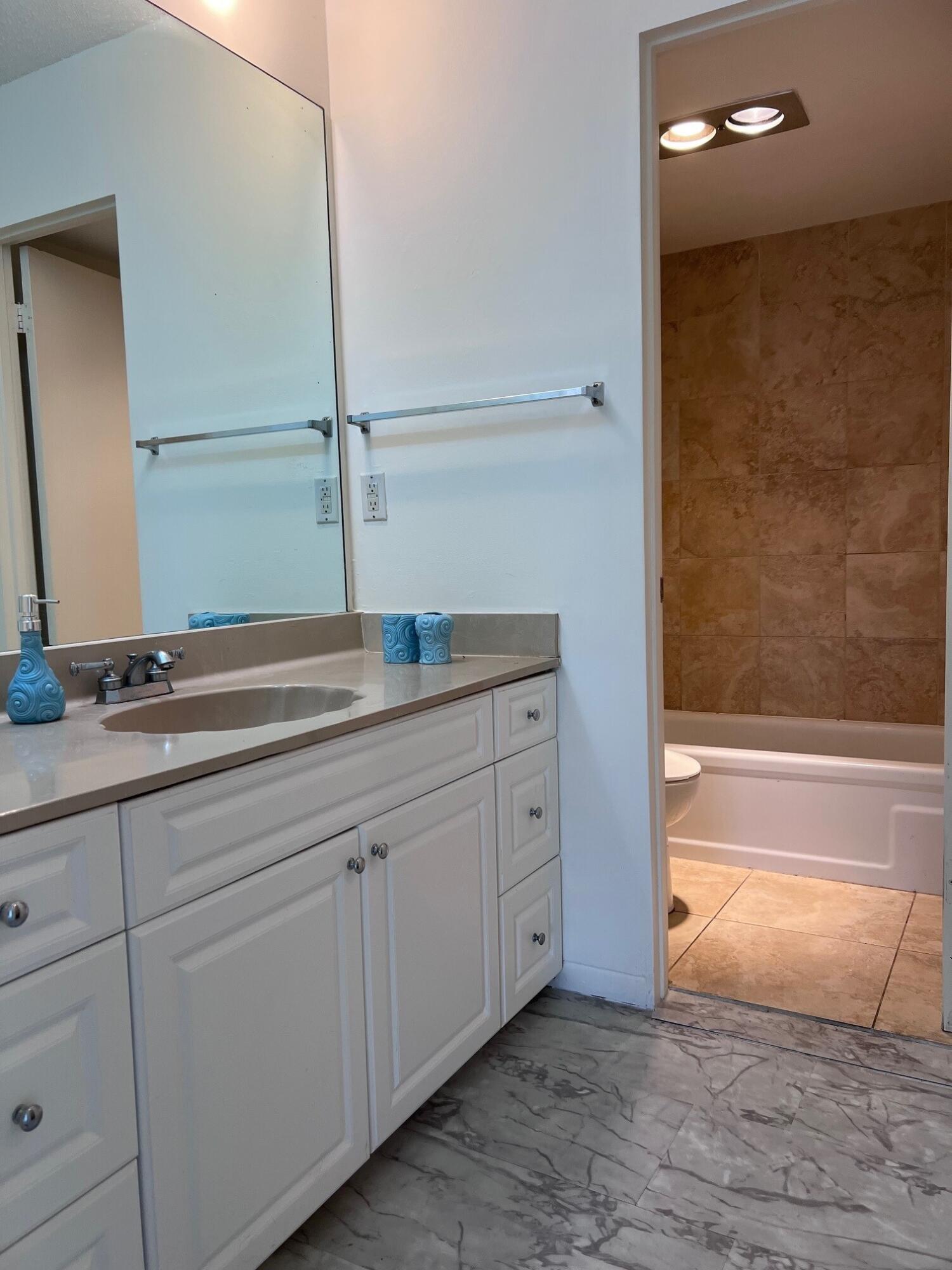 Bathroom with a white vanity, large mirror, and bathtub with a brown tiled surround.