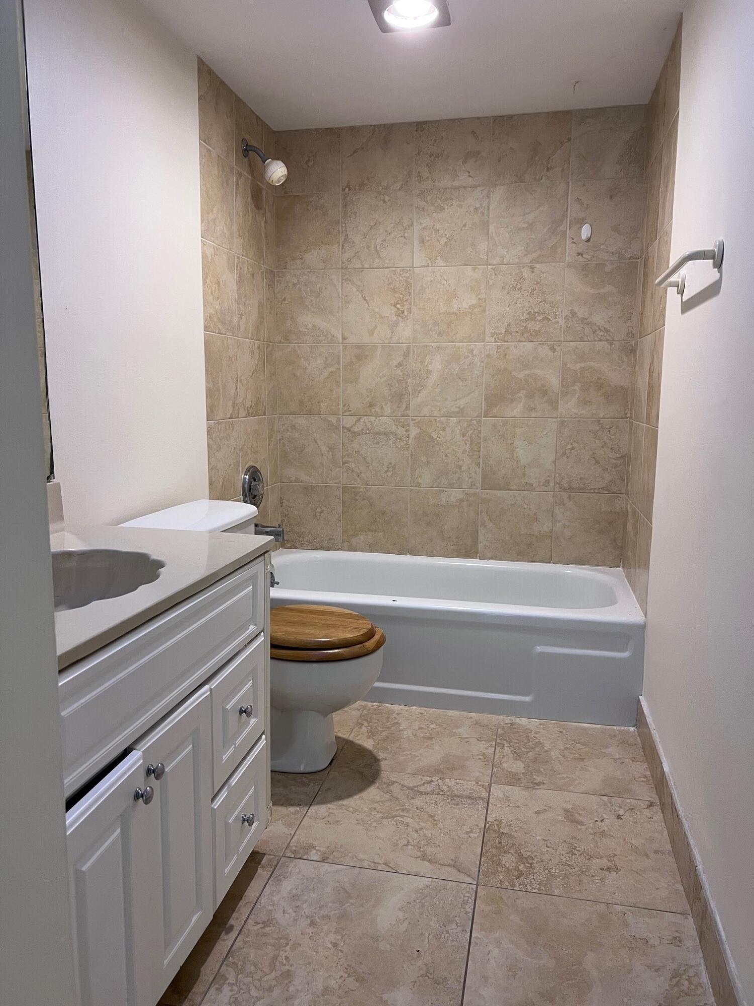 Bathroom with beige tiled tub and shower beside a white vanity and toilet.