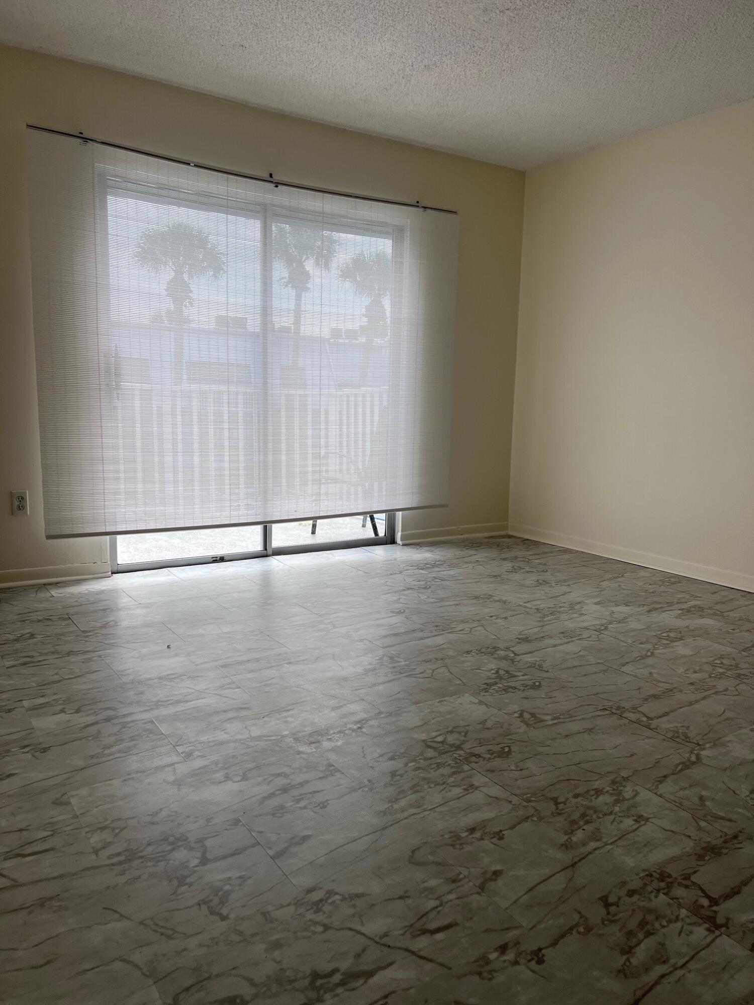 Vacant room with marble-pattern tile floors and a sliding glass door with blinds.