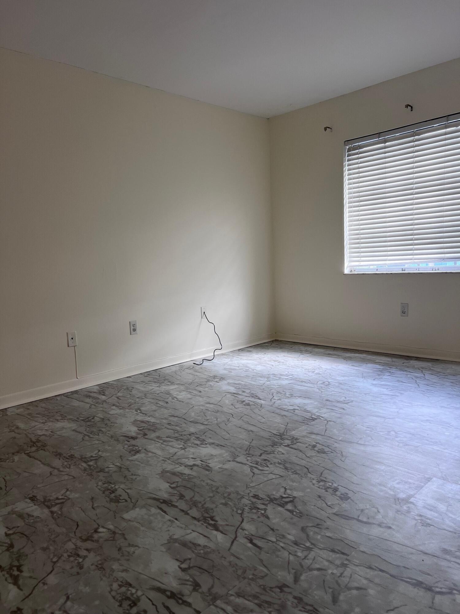 Empty room with gray marble-patterned tile flooring and a window with blinds.