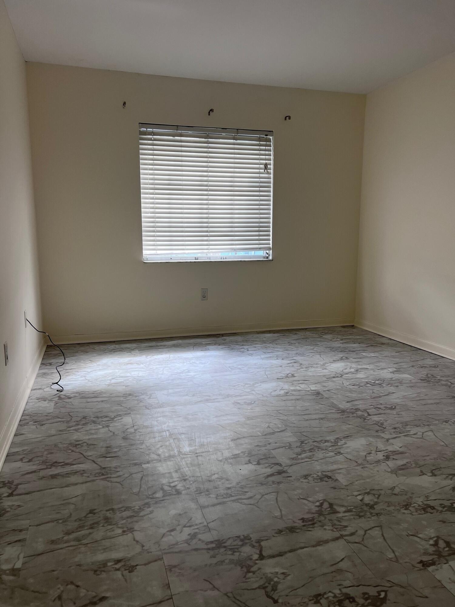 Empty room with marble-pattern tile flooring and a window with closed blinds.