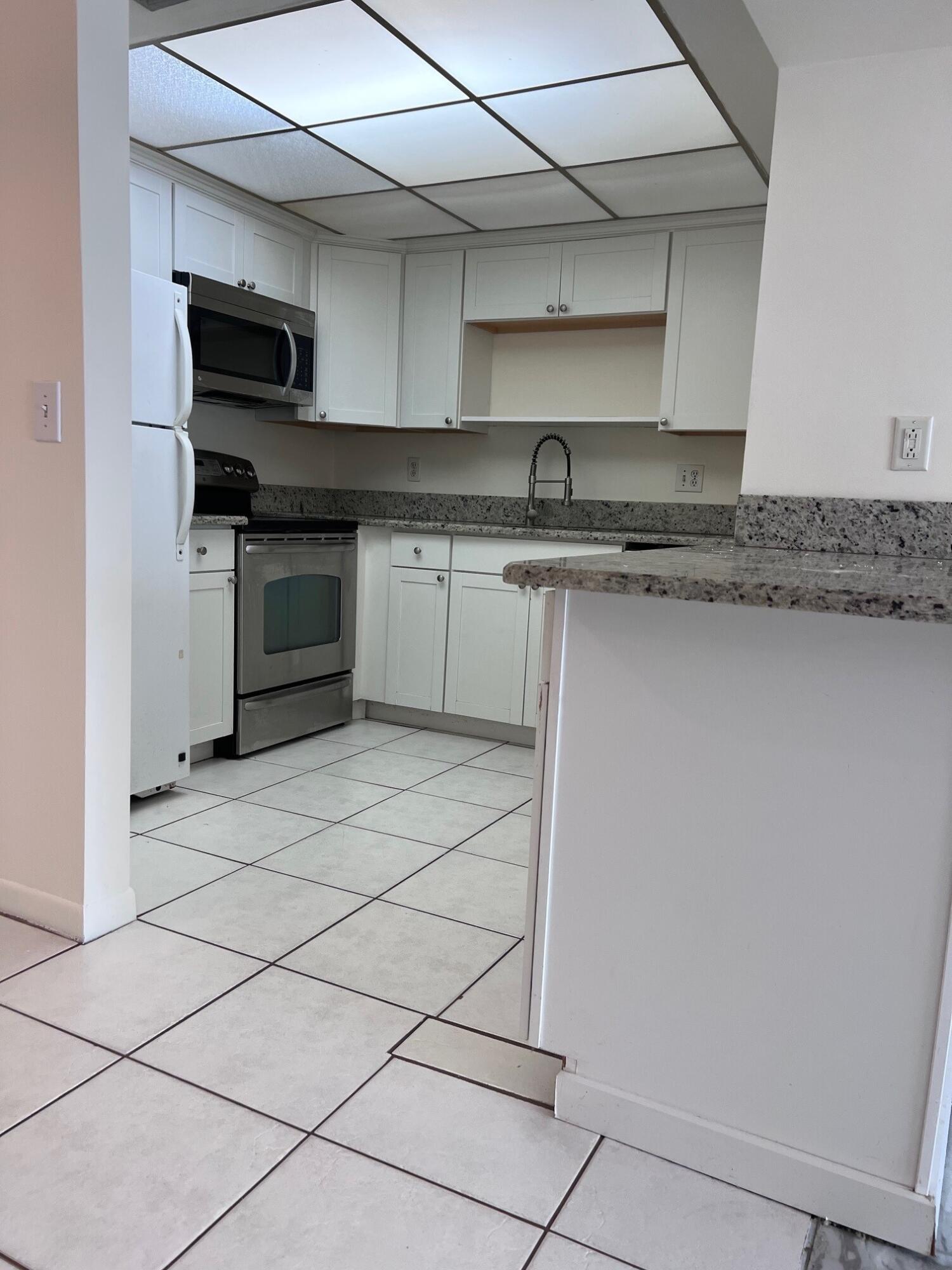 Kitchen with white cabinets, granite counters, tiled floor, and stainless-steel appliances.