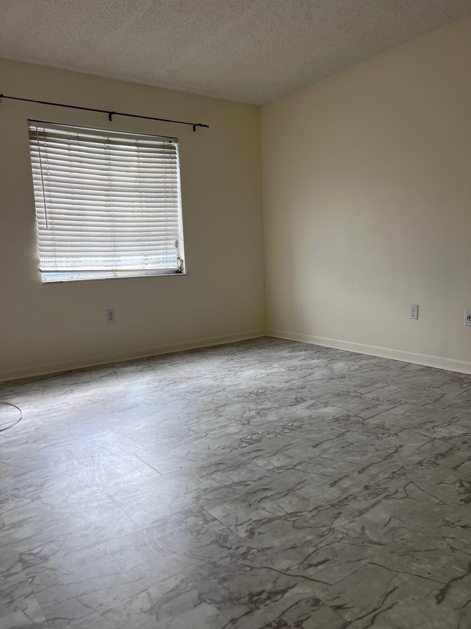 Empty room with marble-patterned tile flooring and a window with white blinds.