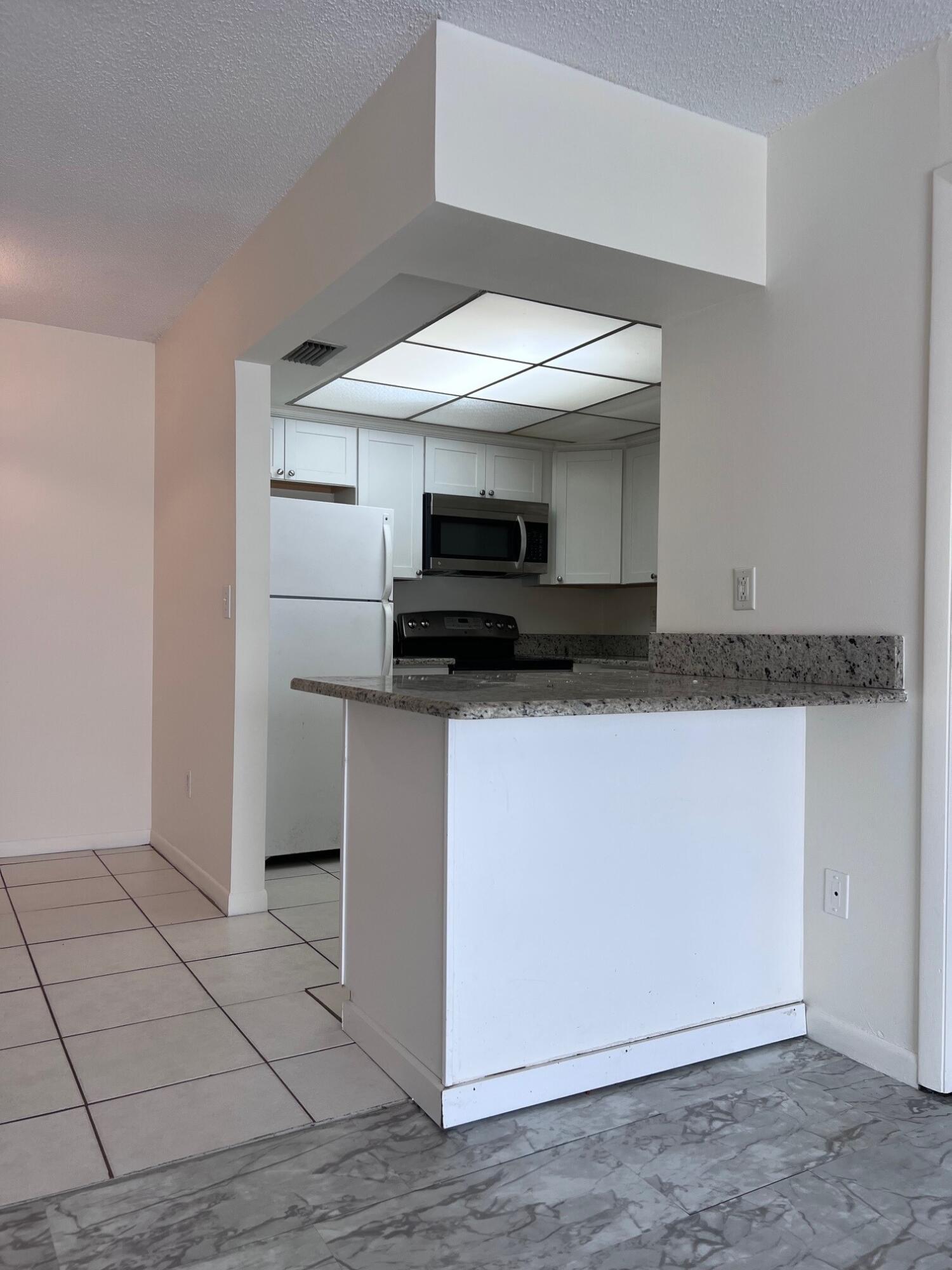 Unfurnished condo kitchen with white cabinets and appliances behind a granite breakfast bar.