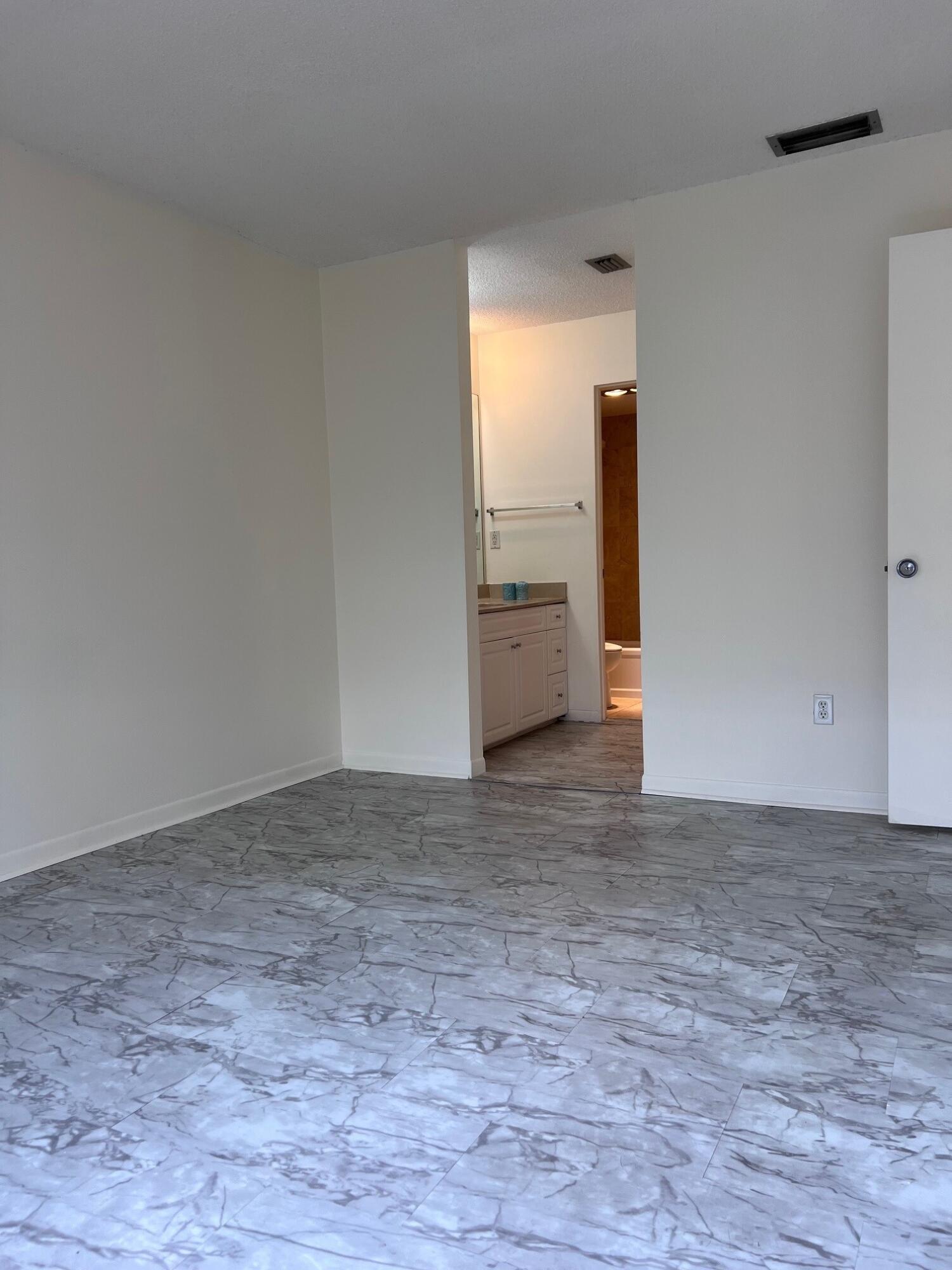 Empty room with gray marble-look tile flooring and an open doorway to a bathroom.
