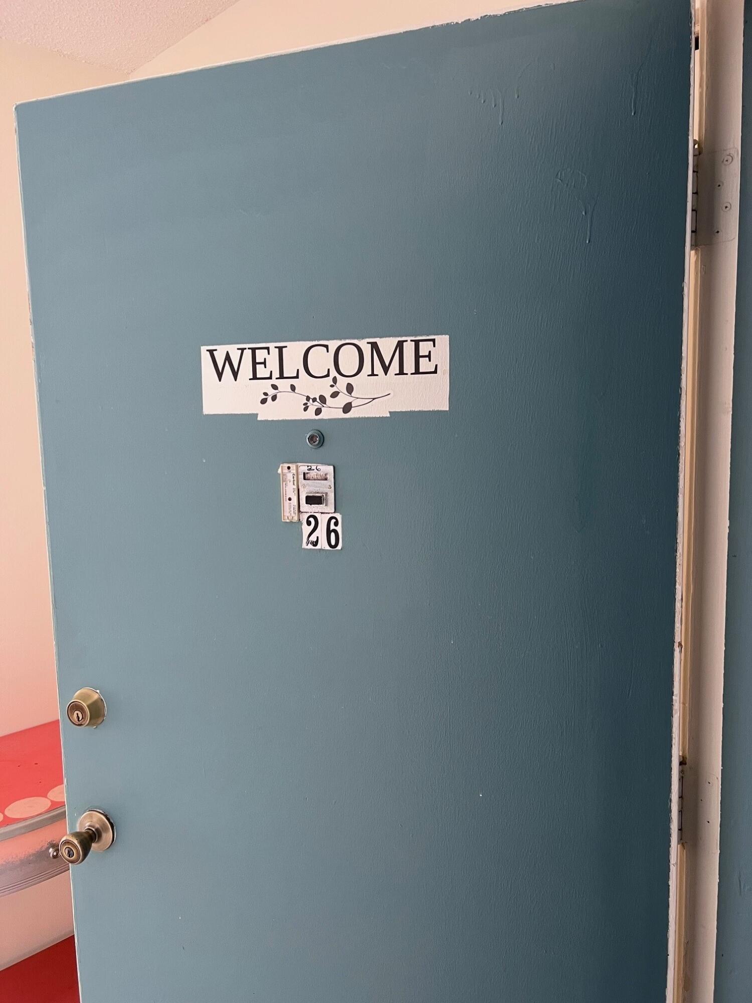 Blue unit 26 door with a welcome sign, peephole, intercom, and brass hardware.