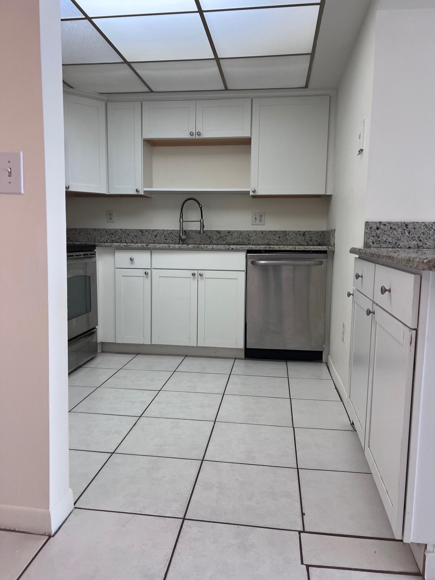 Compact kitchen with white cabinets, granite counters, stainless-steel appliances, and large square tile flooring.
