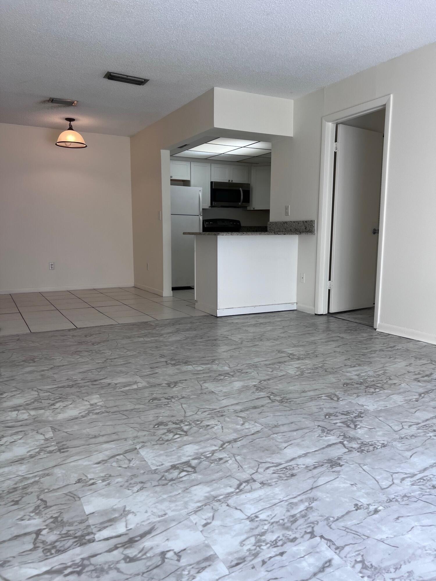 Unfurnished living and dining area with marble-look tile floors and a kitchen breakfast bar.