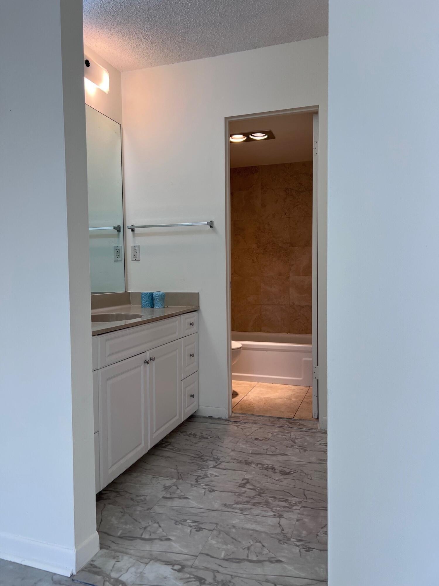 Bathroom with a white vanity, mirrored wall, and brown-tiled tub and shower.