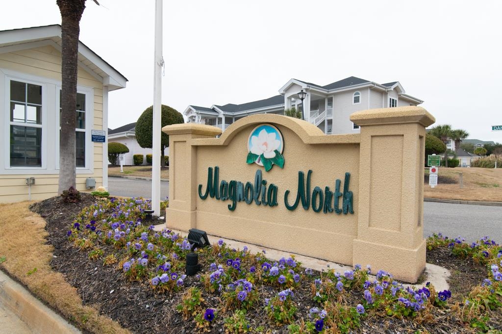 Magnolia North entrance sign with a magnolia emblem and purple flowers.