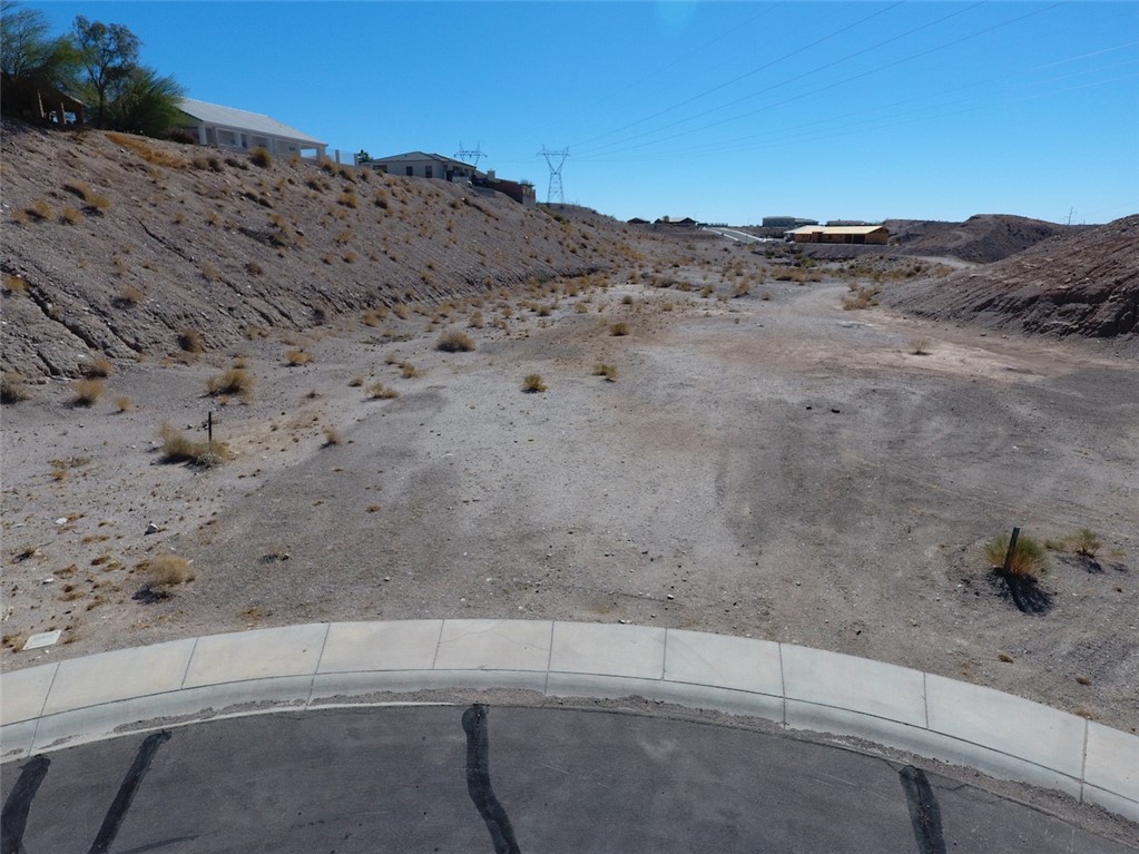Vacant desert lot at a cul-de-sac, with rocky slopes and sparse shrubs.