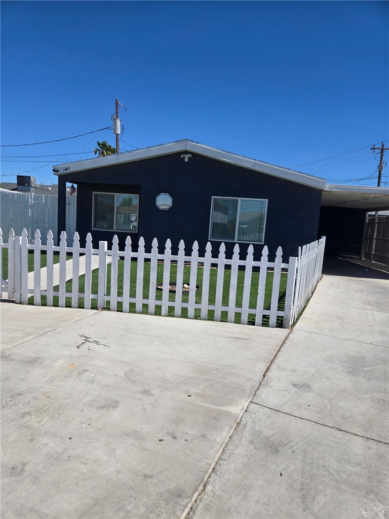 Dark blue single-story house with a white picket fence, small lawn, and covered carport.