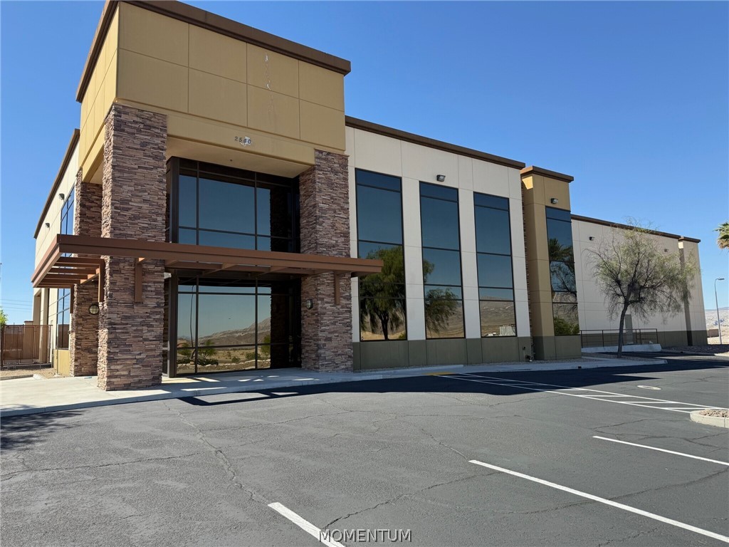 Modern office building with reflective windows, stone accents, and an empty parking lot.