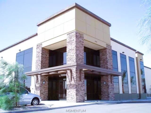 Modern commercial building with stone-clad columns, broad glass windows, and a flat projecting roof.