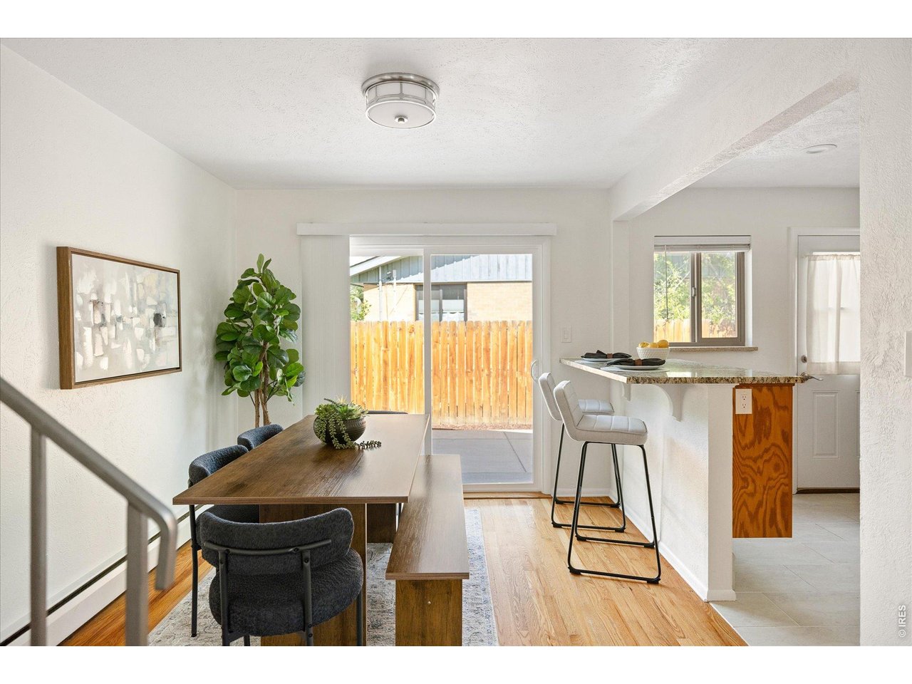 Dining area with a long wood table, breakfast bar, and sliding door to a fenced patio.