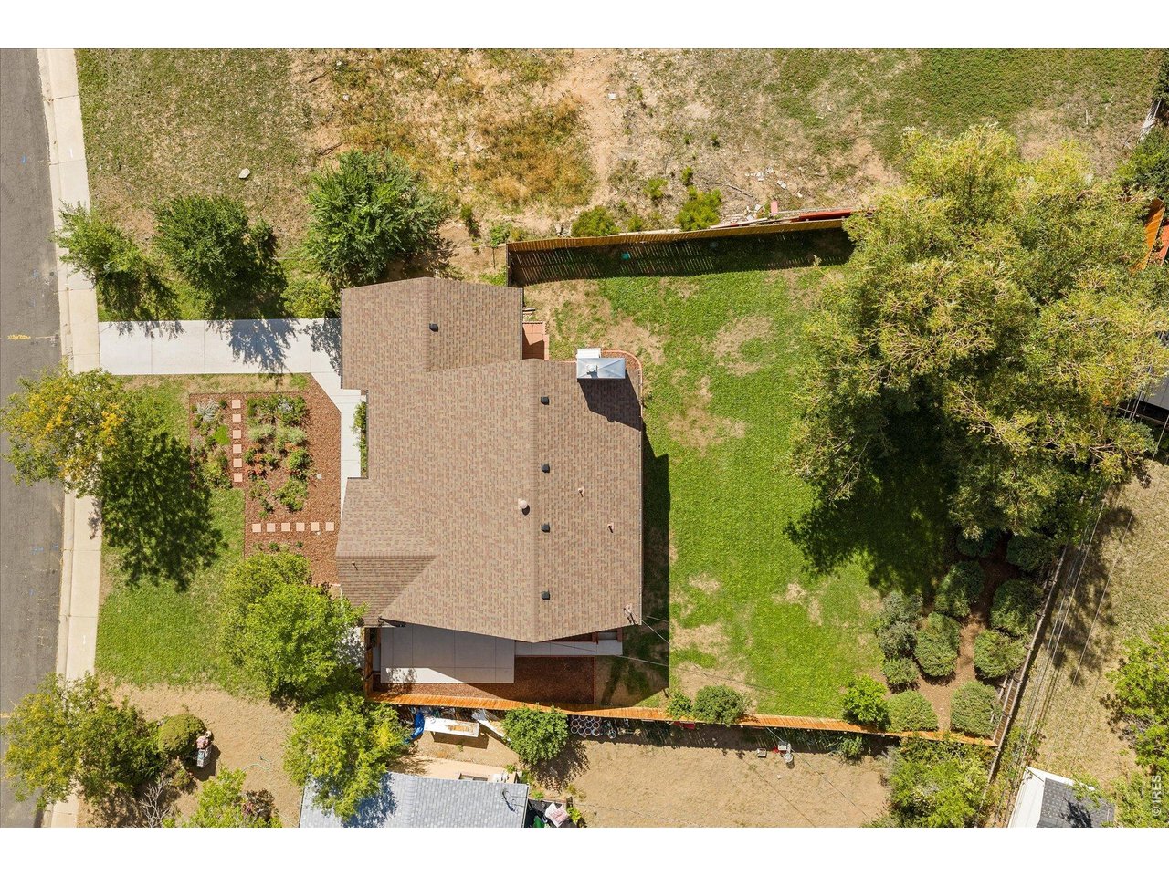Aerial view of a house with a broad shingled roof, fenced lawn, and garden.
