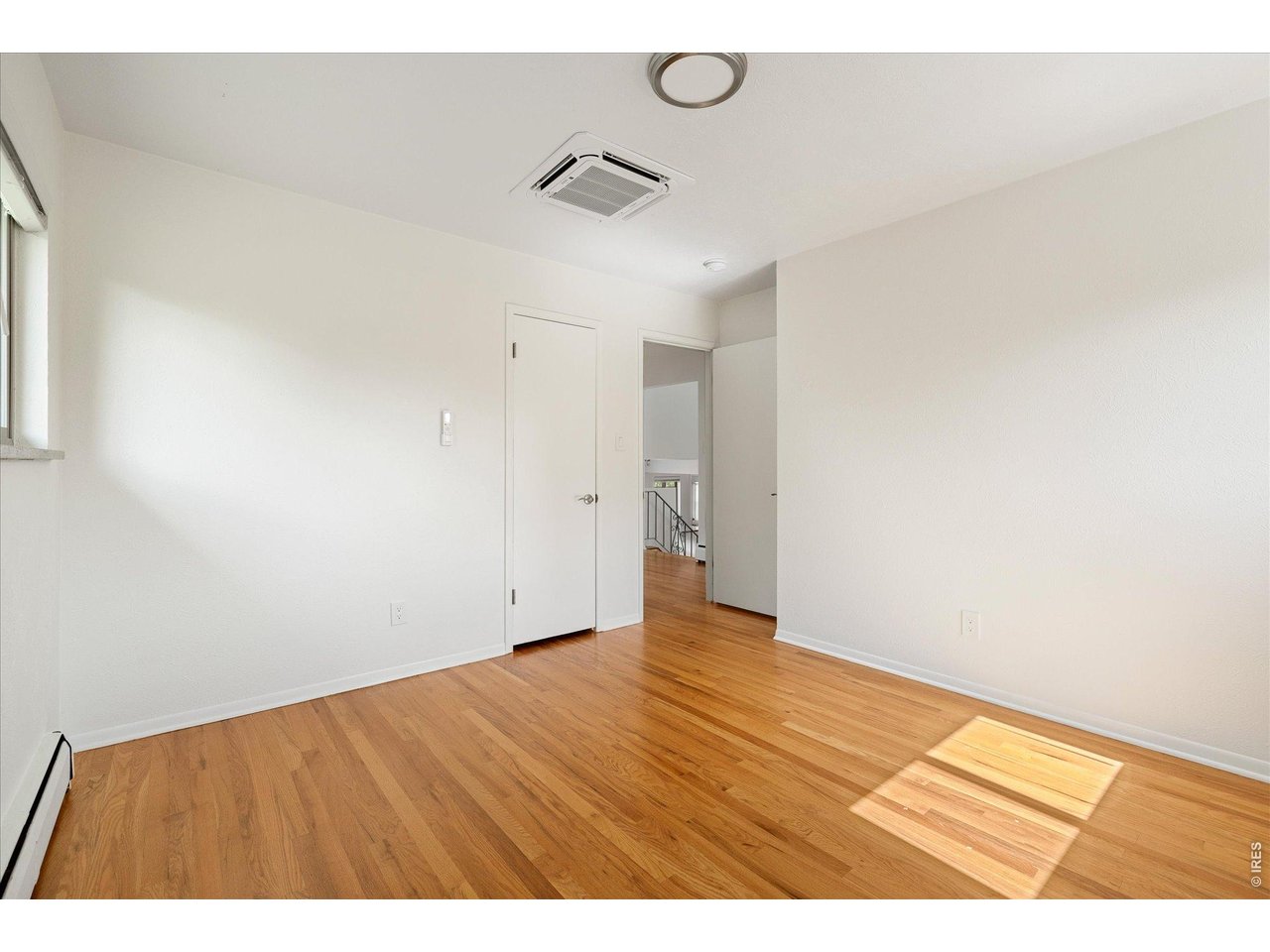 Empty room with hardwood floors, white walls, and sunlight streaming through a window.