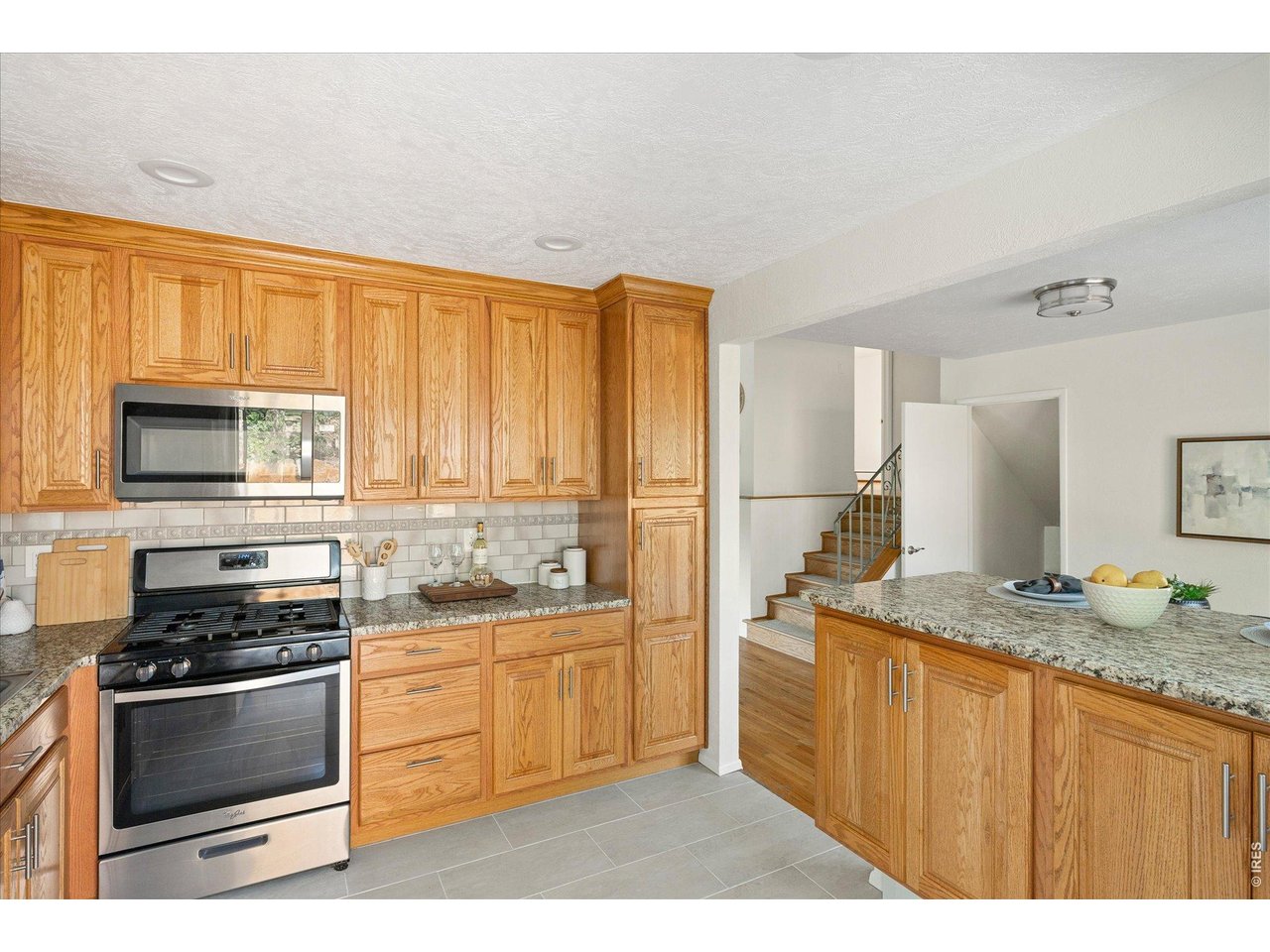 Kitchen with honey-oak cabinets, granite counters, and a stainless-steel gas range beside a fruit-topped island.