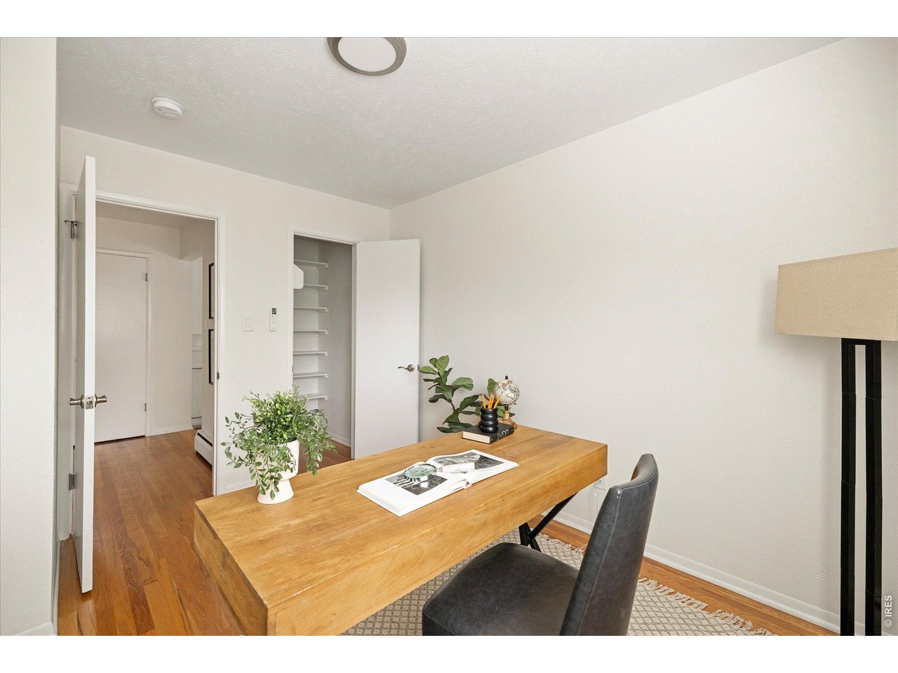 Home office with a large wooden desk, dark chair, and open shelving closet.