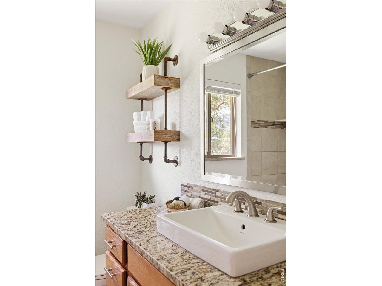 Bathroom vanity with a white rectangular sink, granite counter, and rustic wood shelves beside a large mirror.