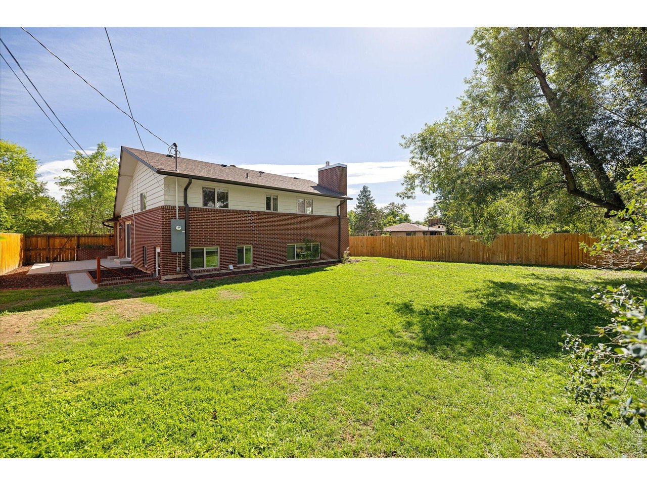 House with red brick lower level and a broad, fenced backyard lawn.
