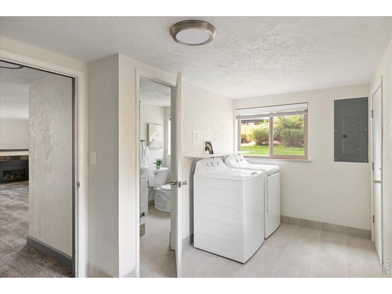 Laundry room with white washer and dryer beneath a window overlooking a green yard.