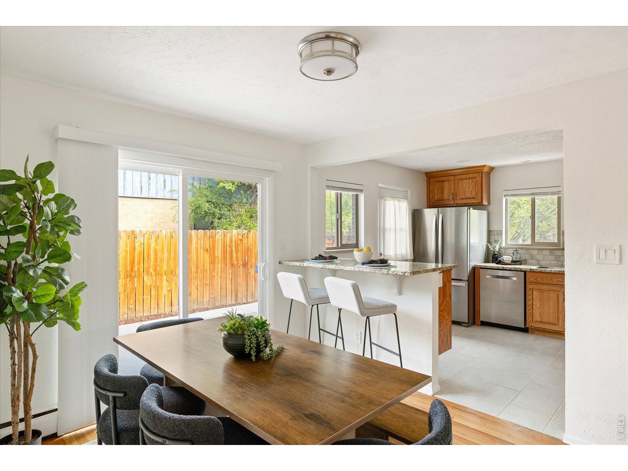 Dining area with a wood table beside an open kitchen and sliding doors to a fenced yard.