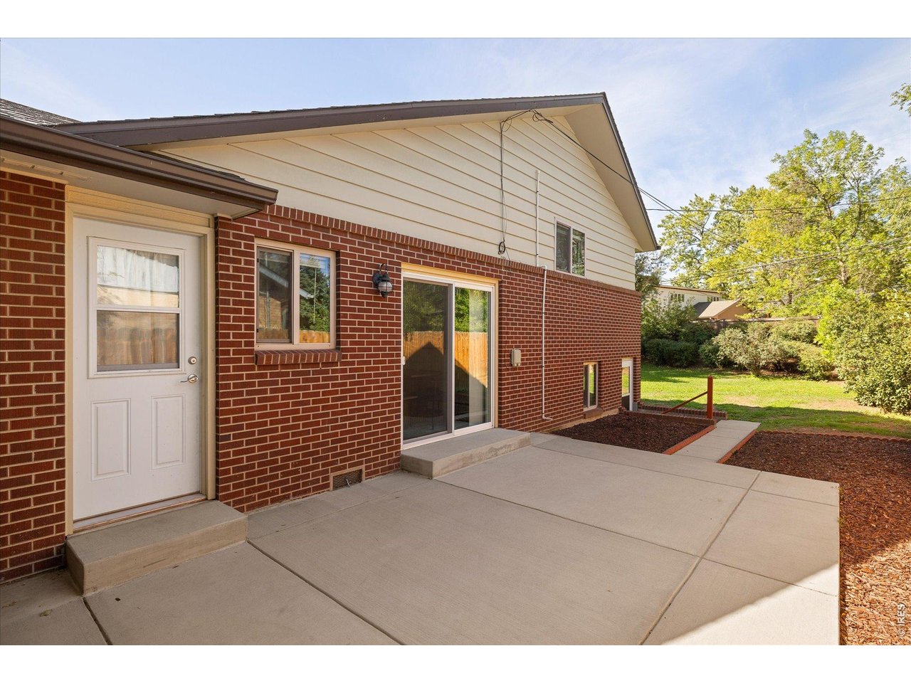 Home exterior with a broad concrete patio, brick walls, and a sliding glass door.