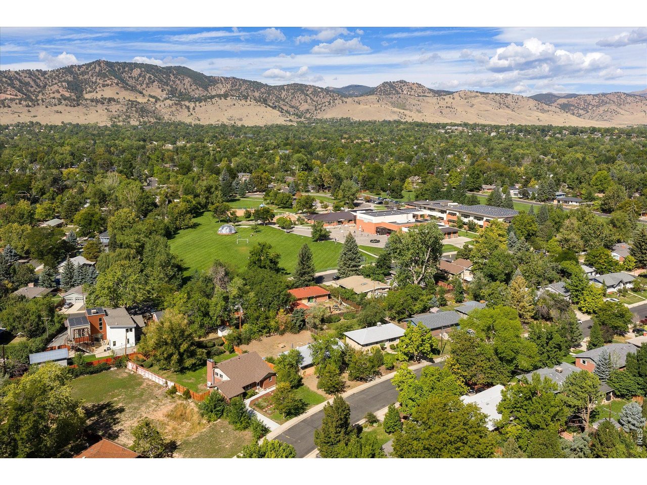 Aerial view of a leafy Boulder neighborhood and playing field beneath the Front Range mountains.