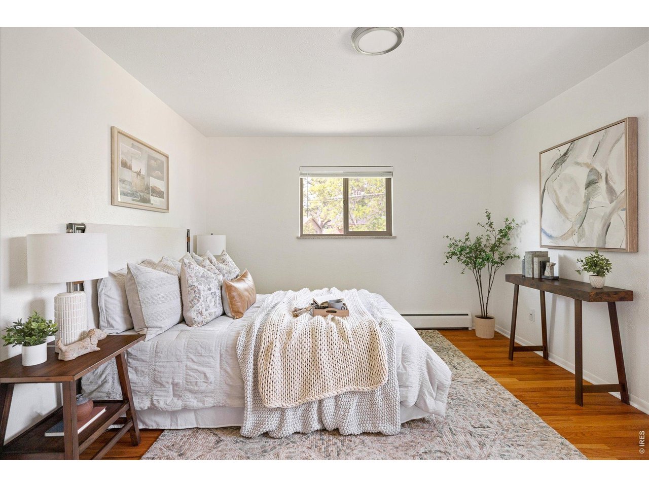 Staged bedroom with a white bed, textured throw, hardwood floors, and a window.