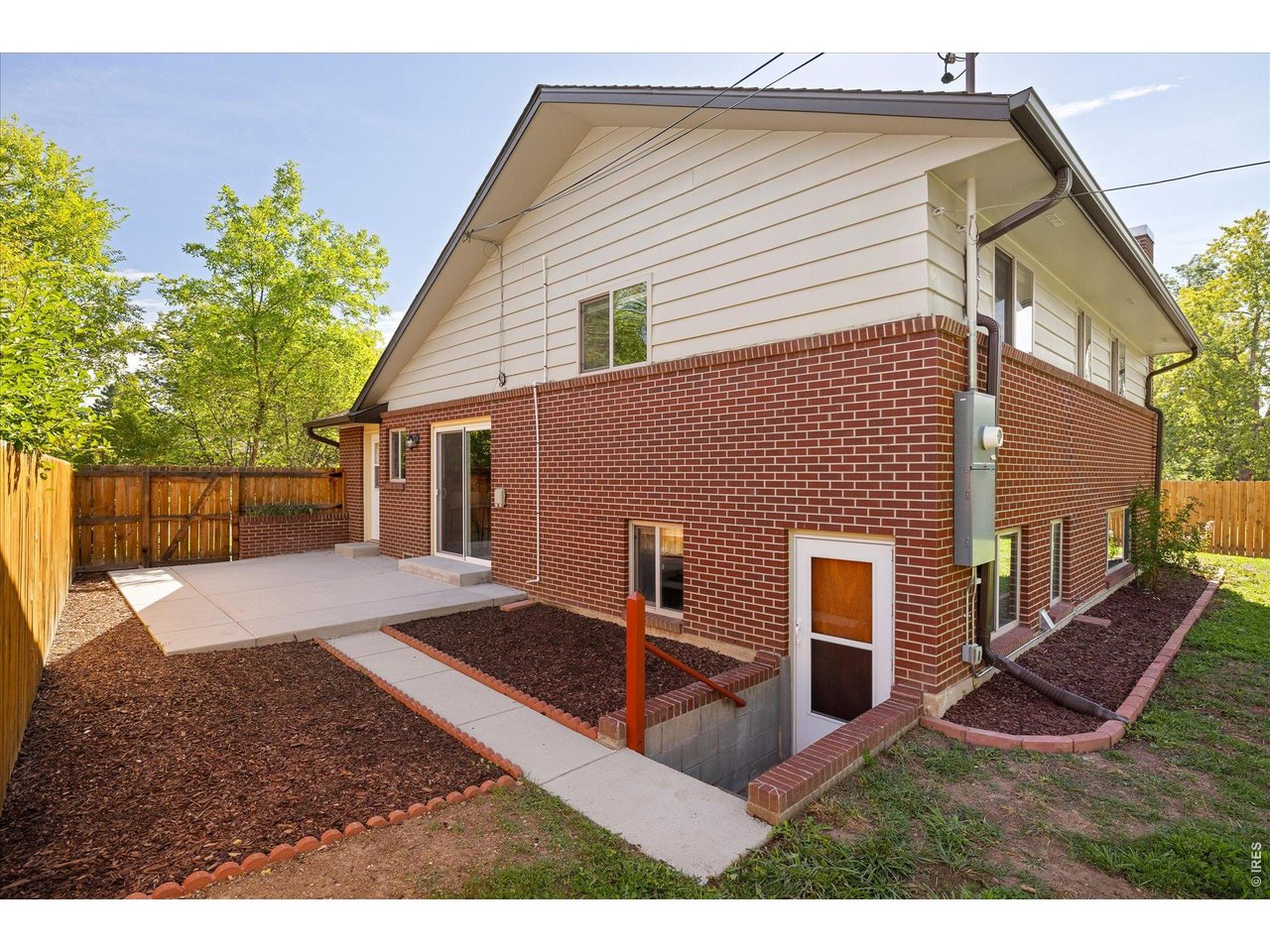 Back of a two-story brick-and-siding house with a concrete patio and fenced, landscaped yard.