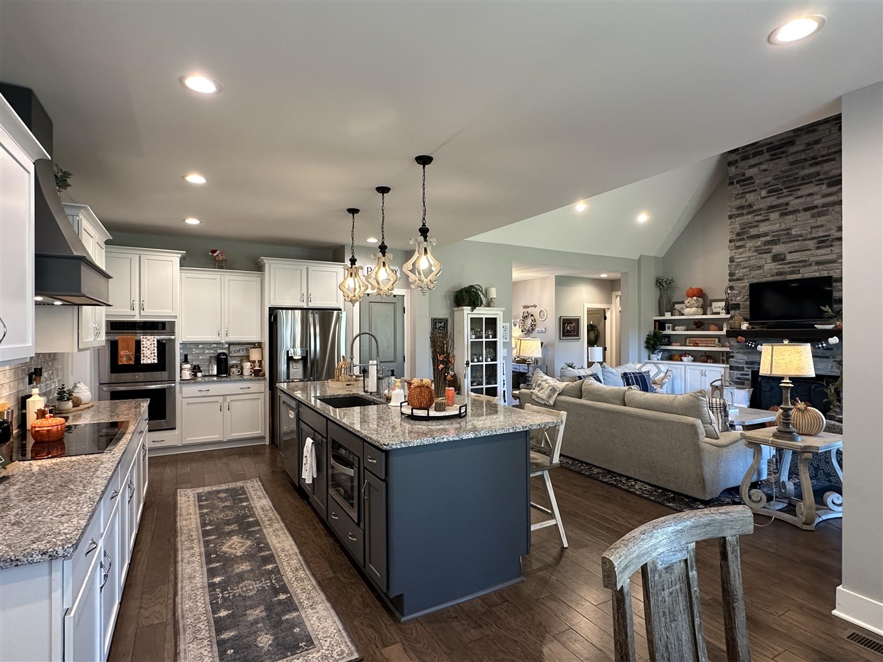Open-plan kitchen and living room with a dark blue island and stone fireplace.