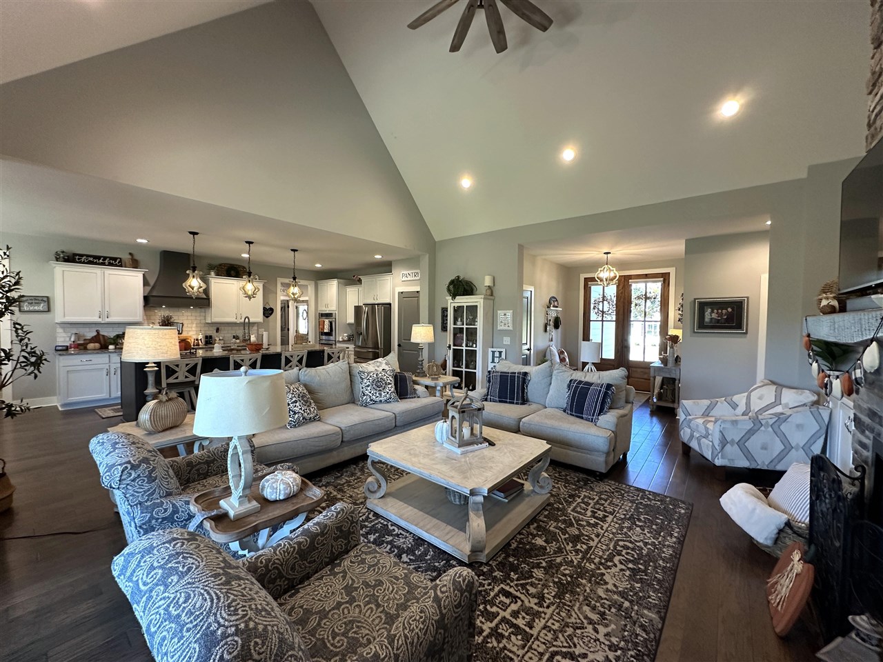 Open-plan living room and kitchen with vaulted ceilings, gray sofas, patterned chairs, and white cabinets.