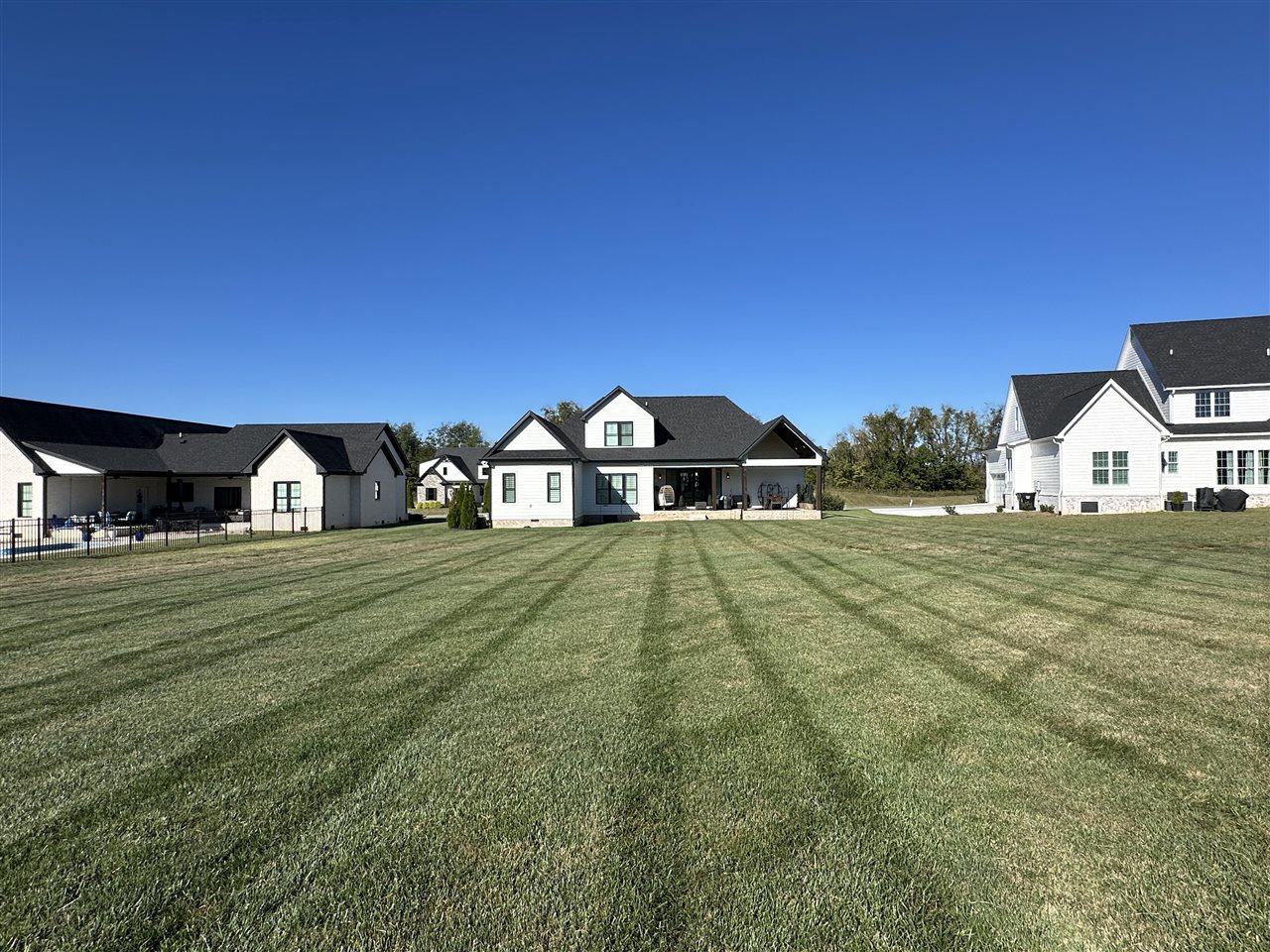 Light-sided house with a dark roof and covered patio beyond a broad mowed lawn.
