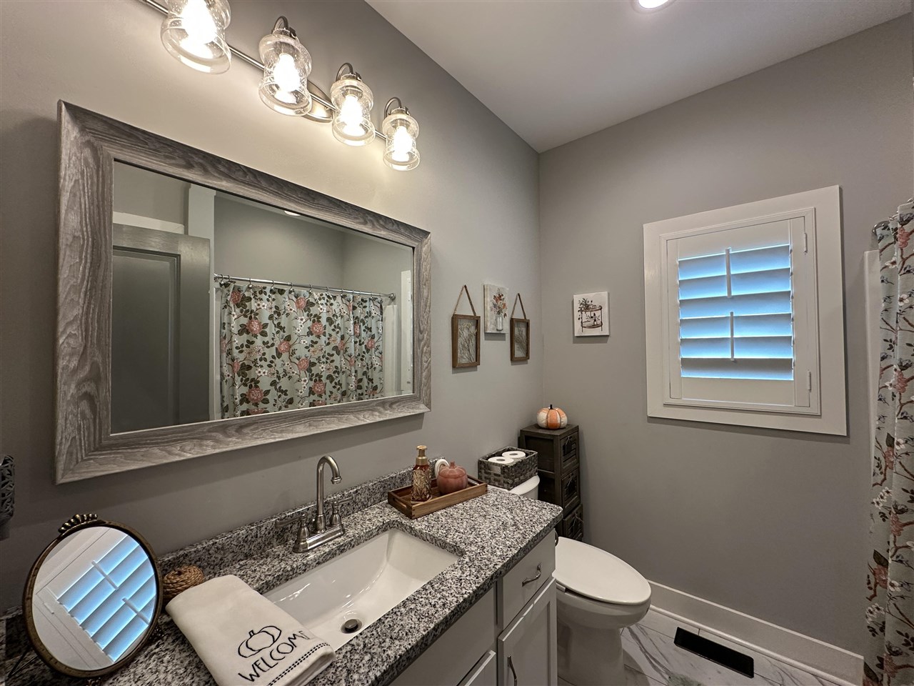 Bathroom with a granite vanity, large framed mirror, and shuttered window.