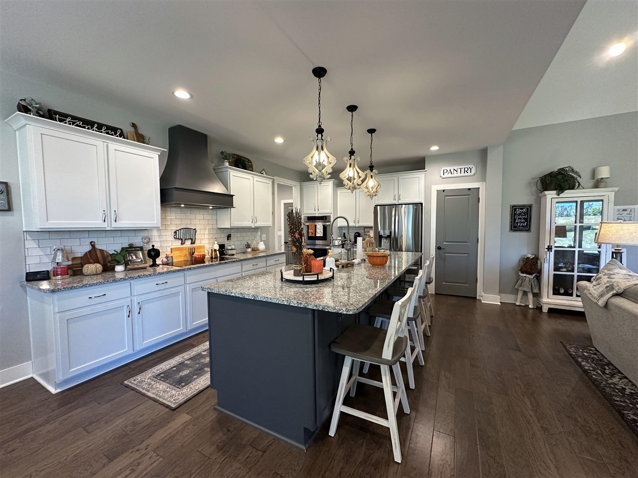 Open-plan kitchen with white cabinets, a large granite island, stainless steel appliances, and pendant lights.