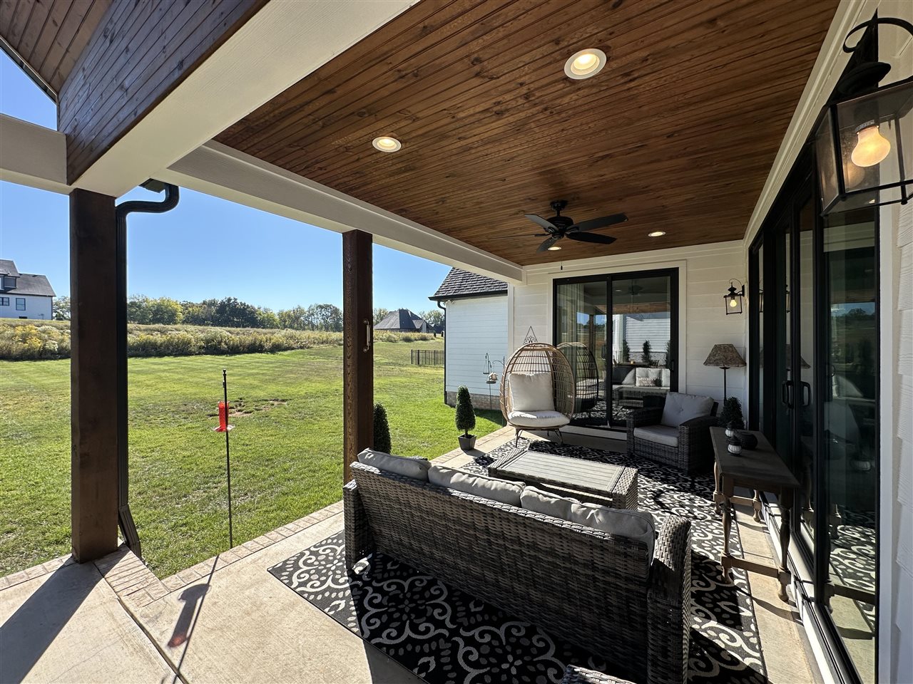 Covered patio with wicker seating and a wood-plank ceiling overlooking a broad lawn.