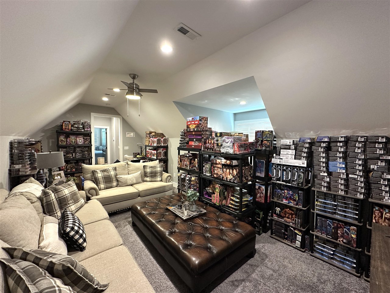 Upstairs bonus room with sloped ceilings, beige sofas, and shelves of boxed collectibles.