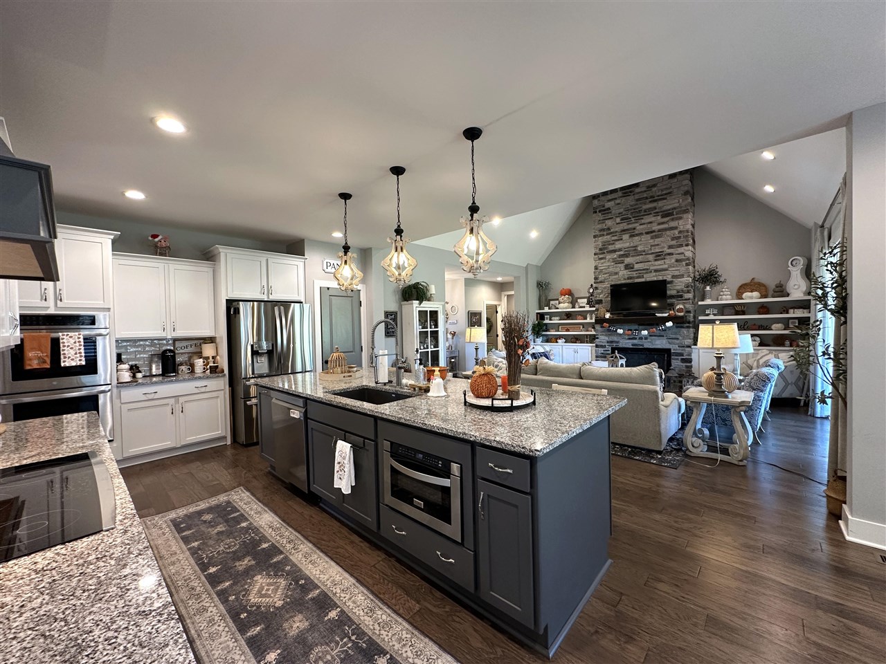 Open-plan kitchen with a large dark island and granite counters, opening onto a living room with a stone fireplace.