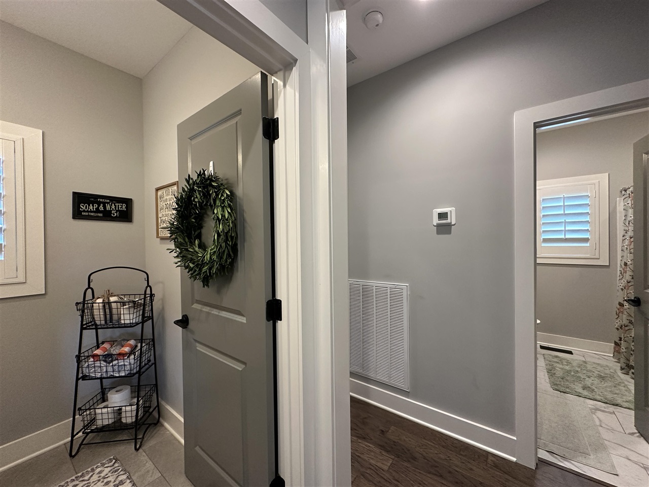 Gray bathroom entry with a wreath-covered door, towel stand, and adjoining tiled bathroom.