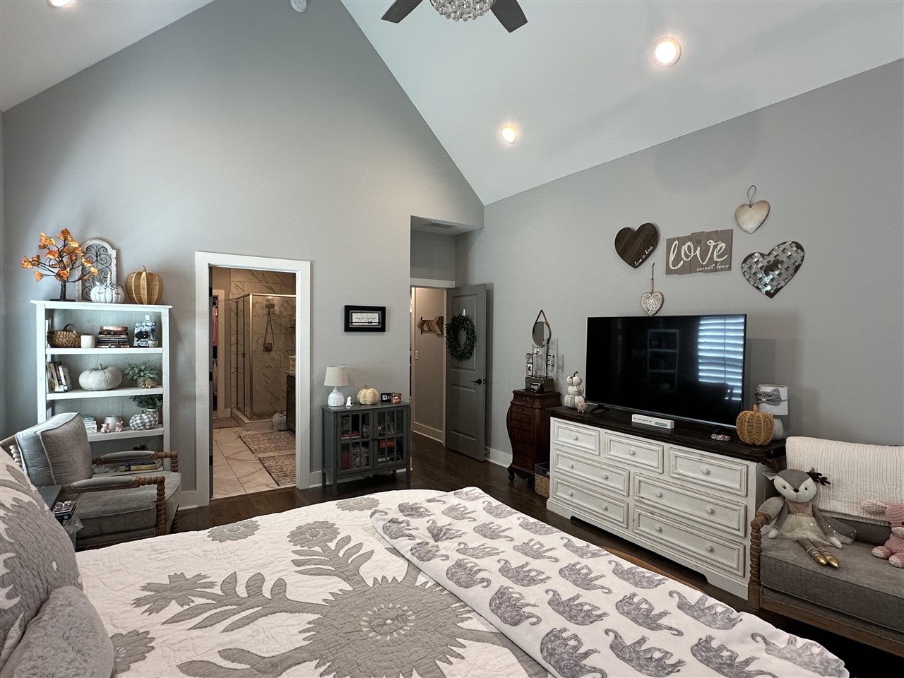 Furnished bedroom with a vaulted ceiling, patterned bedspread, and doorway to a tiled bathroom.