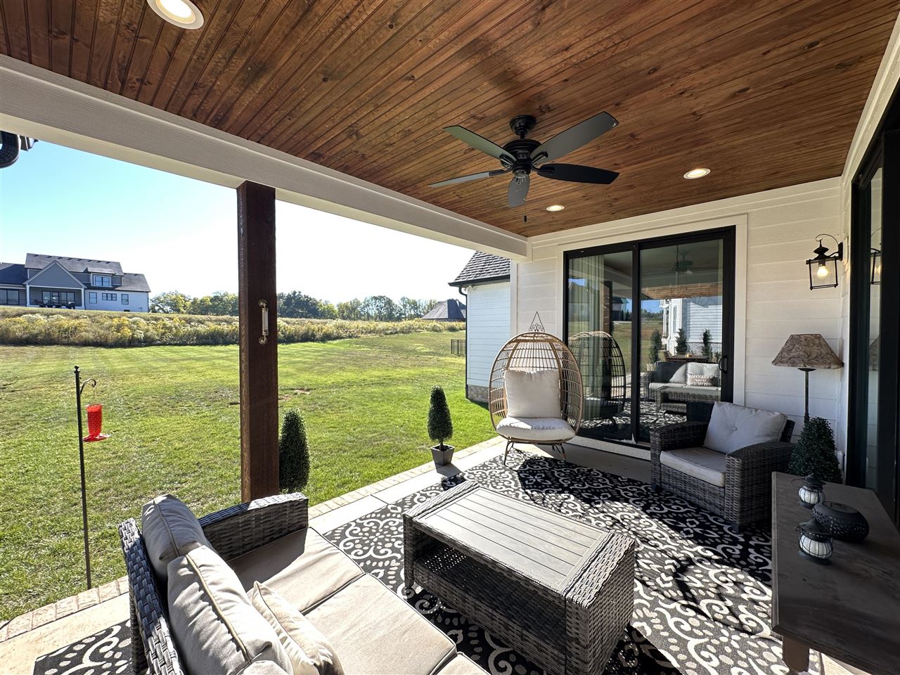 Covered patio with wicker seating and a wood-plank ceiling overlooking a green lawn.