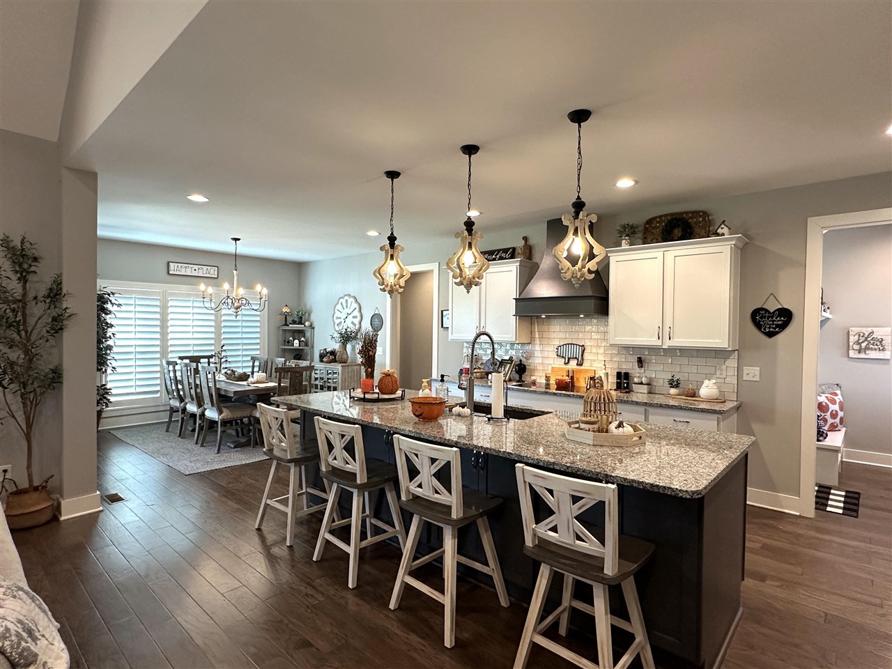 Open kitchen with a granite island and white bar stools beside a dining area.